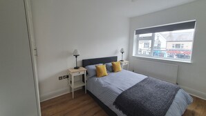 Une chambre à coucher avec un lit, deux tables de chevet, une fenêtre et une vue sur les bâtiments environnants.