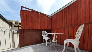 Une terrasse extérieure avec un mur en bois, deux chaises blanches et une petite table.