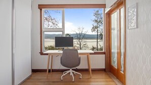 Ein Zimmer mit Schreibtisch, Stuhl und einem großen Fenster mit Blick auf eine Landschaft.