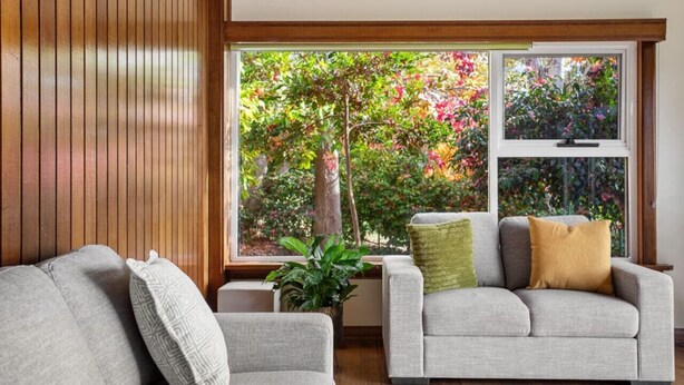 Ein Wohnzimmer mit einer Couch, einem Couchtisch und einem großen Fenster mit Blick auf einen Baum und einen Garten.