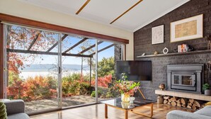 Ein modernes Wohnzimmer mit einem großen Glasschaufenster, das einen herrlichen Ausblick bietet, einem Kamin und einem Flachbildfernseher.