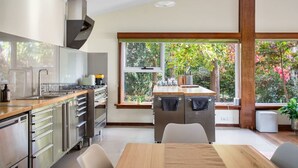 Eine moderne Küche mit Edelstahlgeräten, einer Holzarbeitsplatte und großen Fenstern mit Blick auf Grünflächen.