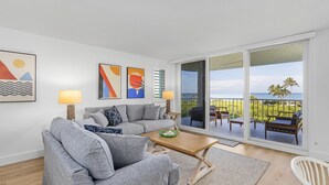 En moderne stue med en grå sofa, et træbord og havudsigt gennem store skydedøre.