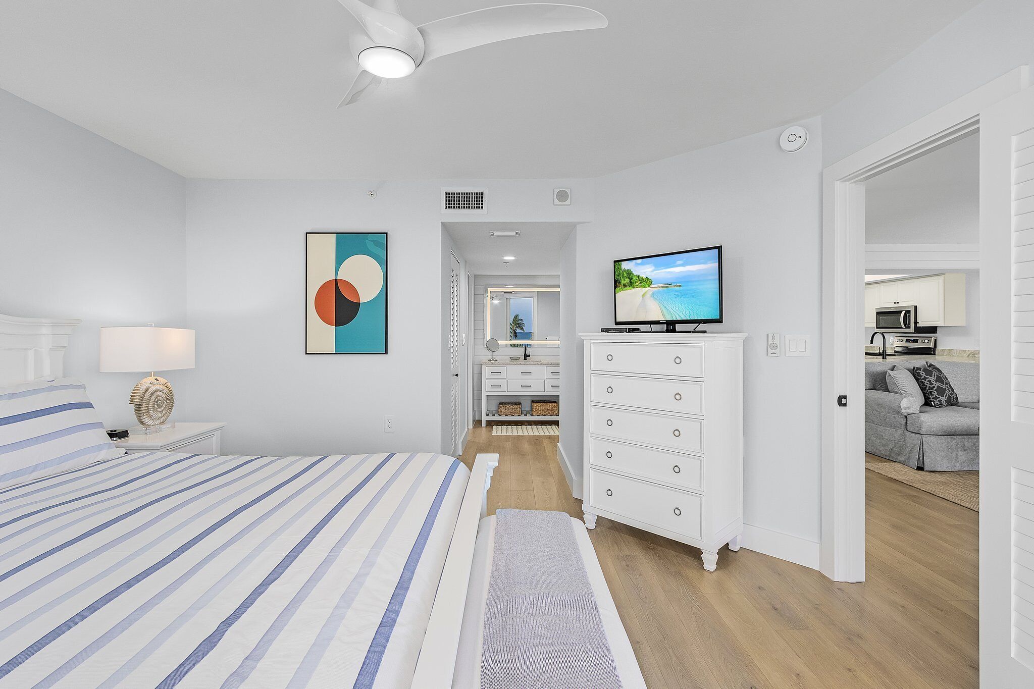 Une chambre à coucher moderne avec un lit, une télévision, une commode et une vue sur la cuisine.
