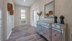 A hallway with a wooden floor, a glass door, a white cabinet with drawers, and a mirror on the wall. - Last Minute Disney! Private Pool, Hot Tub, Game Room & Themed Bedrooms. Book Now! #110895 (Orlando)