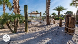 Ein Sandstrand mit Palmen, einer Hängematte und einer Holzkonstruktion.