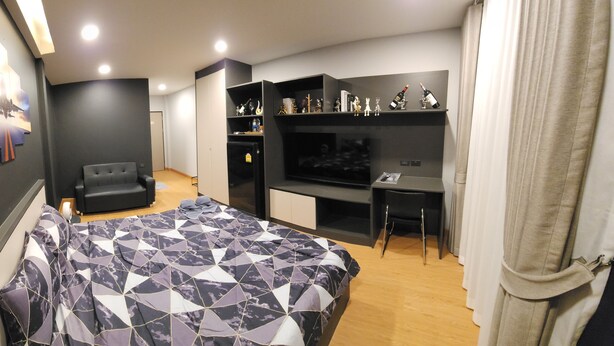 A modern hotel room with a bed, a TV, a seating area, and a minibar.