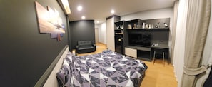A modern hotel room with a bed, a TV, a seating area, and a minibar.