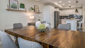 A modern kitchen with white cabinets, a central island, and a dining area with a wooden table and grey chairs. - Last Minute Disney Getaway! Luxury Condo with Private Balcony. Book Now! #105363 (Orlando)
