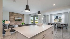 A modern kitchen with a large island, pendant lighting, and a dining area with a table and chairs. - Last Minute Disney Getaway! Luxury Condo with Private Balcony. Book Now! #105363 (Orlando)