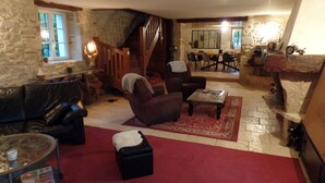 A cozy living room with a stone wall, a wooden staircase, a dining area, and a small kitchen. - Mas Laborde (Mauroux)