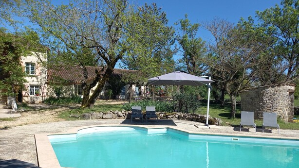 A swimming pool with lounge chairs and an umbrella, surrounded by trees and a stone building. - Mas Laborde (Mauroux)