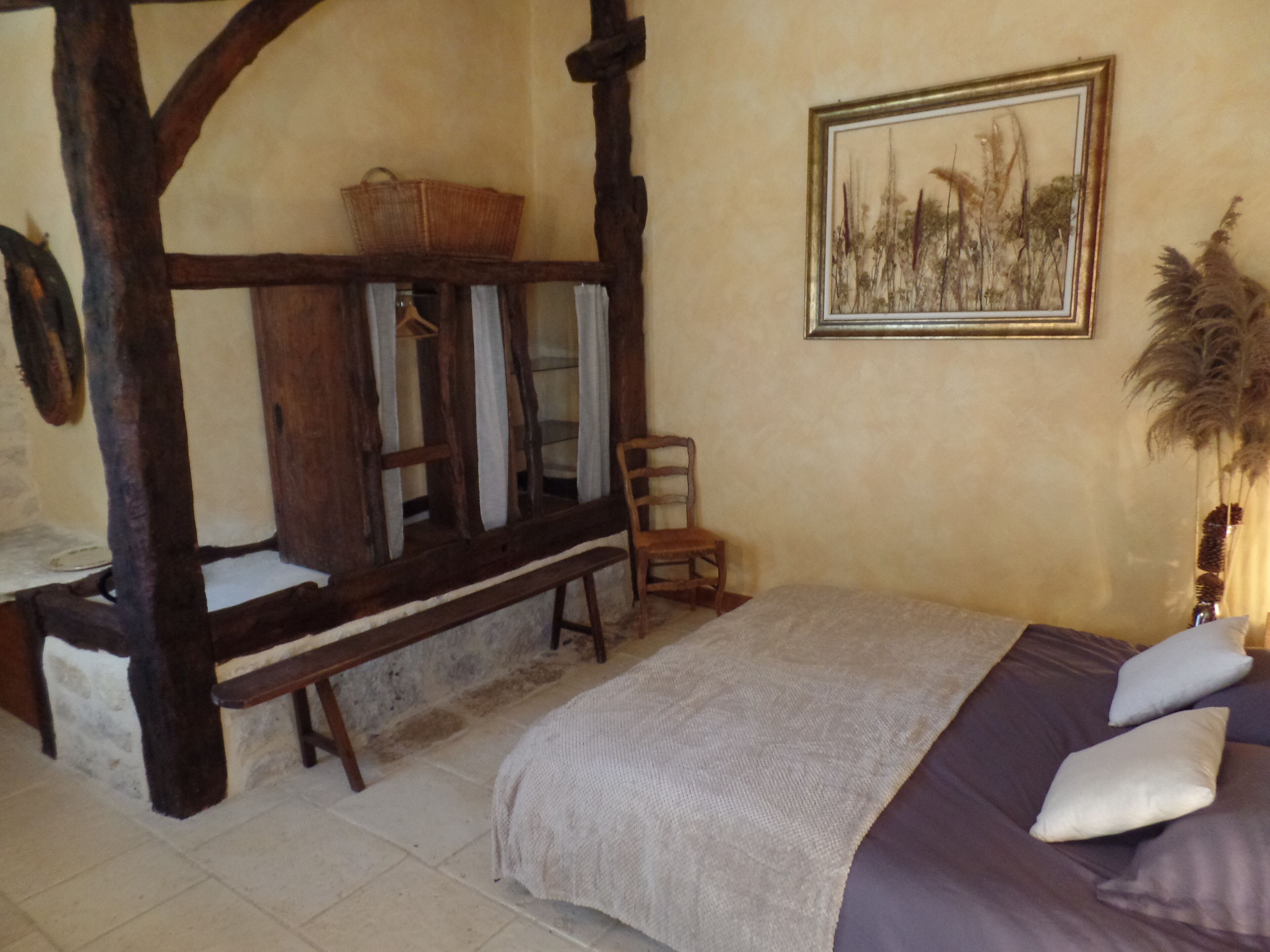 Une chambre à coucher avec un lit à baldaquin, un banc en bois, une chaise et un tableau encadré accroché au mur.