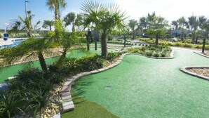Um campo de golfe com putting green, rodeado por palmeiras e vegetação.