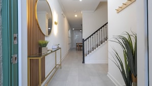 Um corredor com escada, espelho redondo e mesa de apoio com objetos decorativos.