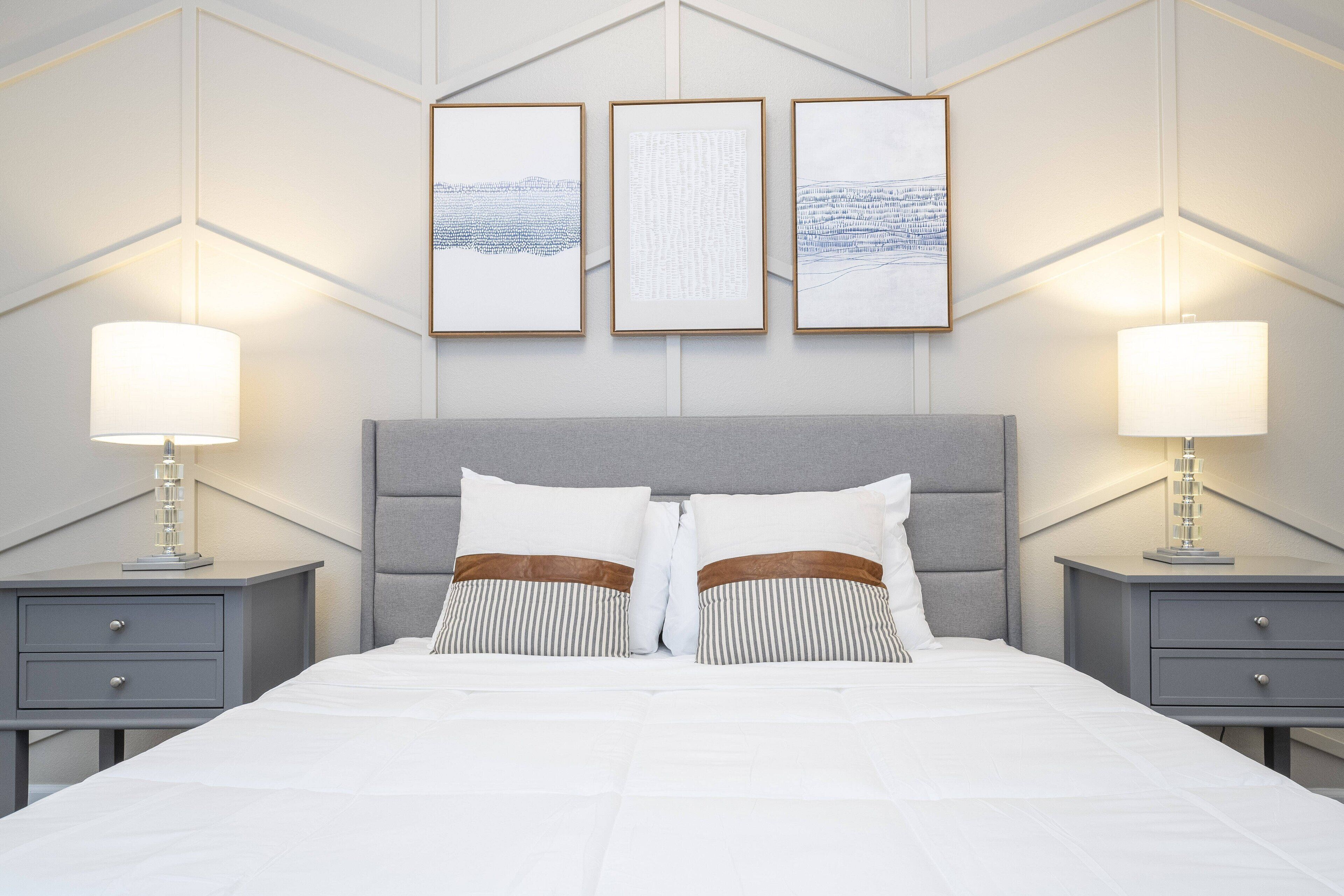 A neatly arranged bedroom with a large bed, two bedside tables with lamps, and three framed artworks on the wall.