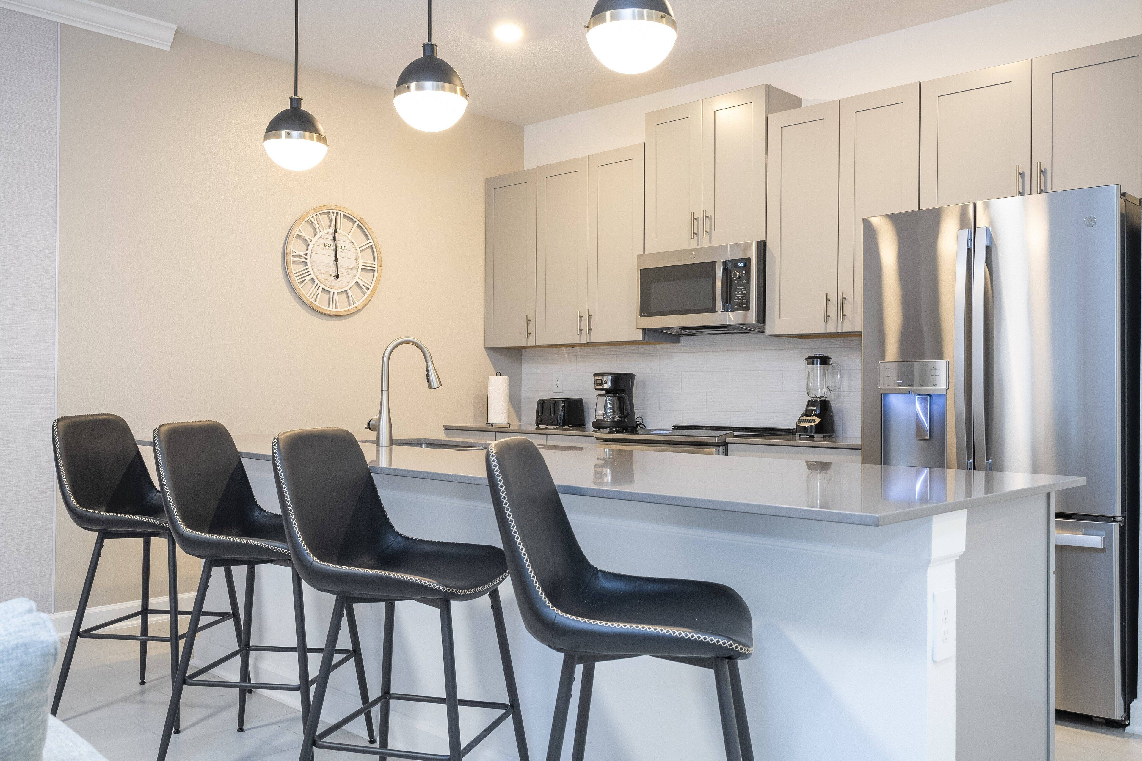 A modern kitchen with a central island, stainless steel appliances, and black bar stools.