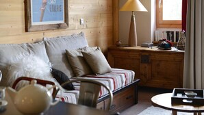 A cozy room with a wooden wall, a sofa with striped cushions, a lamp, and a small table with a tray. - 100m from resort center, 6th floor, view ski slopes, terrace, balcony, tv, ski locker, 57m² (La Plagne)