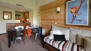 A cozy room with a wooden wall, a dining area with chairs and a table, and a sofa with striped bedding. - 100m from resort center, 6th floor, view ski slopes, terrace, balcony, tv, ski locker, 57m² (La Plagne)