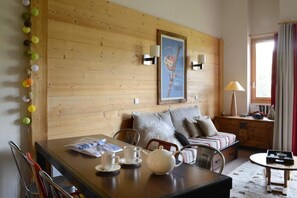 Une pièce chaleureuse avec un mur en bois, un lit avec des oreillers, une table avec des tasses et une théière, et une lampe.