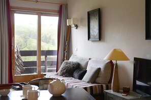 Une pièce confortable avec un canapé, une table avec des tasses et une théière, un téléviseur et une fenêtre avec des rideaux.