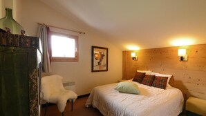 A bedroom with a bed, a chair, a wooden headboard, a wall-mounted light, and a window with curtains. - 100m from resort center, 6th floor, view ski slopes, terrace, balcony, tv, ski locker, 57m² (La Plagne)