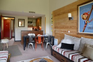 Un salon chaleureux avec un canapé à rayures, une table à manger entourée de chaises et, au fond, une cuisine.