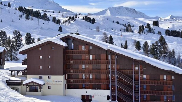 A multi-story lodge with a ski slope in the background. - 100m from resort center, 6th floor, view ski slopes, terrace, balcony, tv, ski locker, 57m² (La Plagne)