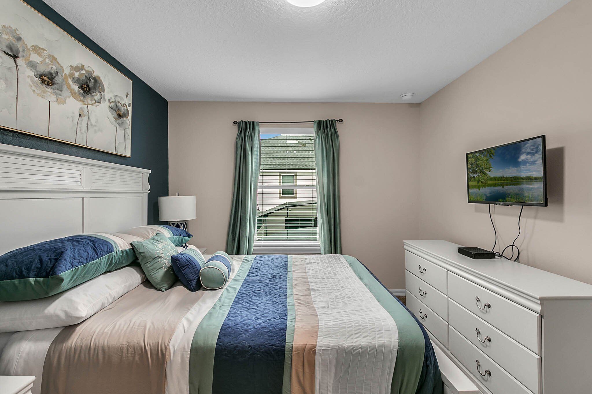 Een slaapkamer met een bed, een dressoir, een televisie en een raam met gordijnen.