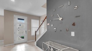 Un intérieur moderne avec une horloge murale grise, un escalier et une porte dotée d’une petite fenêtre.