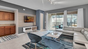 Un salon moderne avec un canapé, une table basse et un téléviseur. Il y a également un coin cuisine équipé de placards et d’un plan de travail.