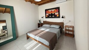Une chambre avec un plafond en bois, un lit recouvert d’une couvre-lit à motifs, un climatiseur fixé au mur et une œuvre d’art encadrée.