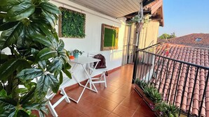 Un balcon avec une table et des chaises blanches, des plantes en pot et un sol carrelé.