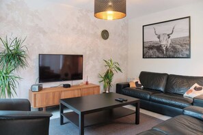 Ein modernes Wohnzimmer mit Flachbildfernseher, einem schwarzen Ledersofa, einem Holzkabinett und einem Couchtisch.