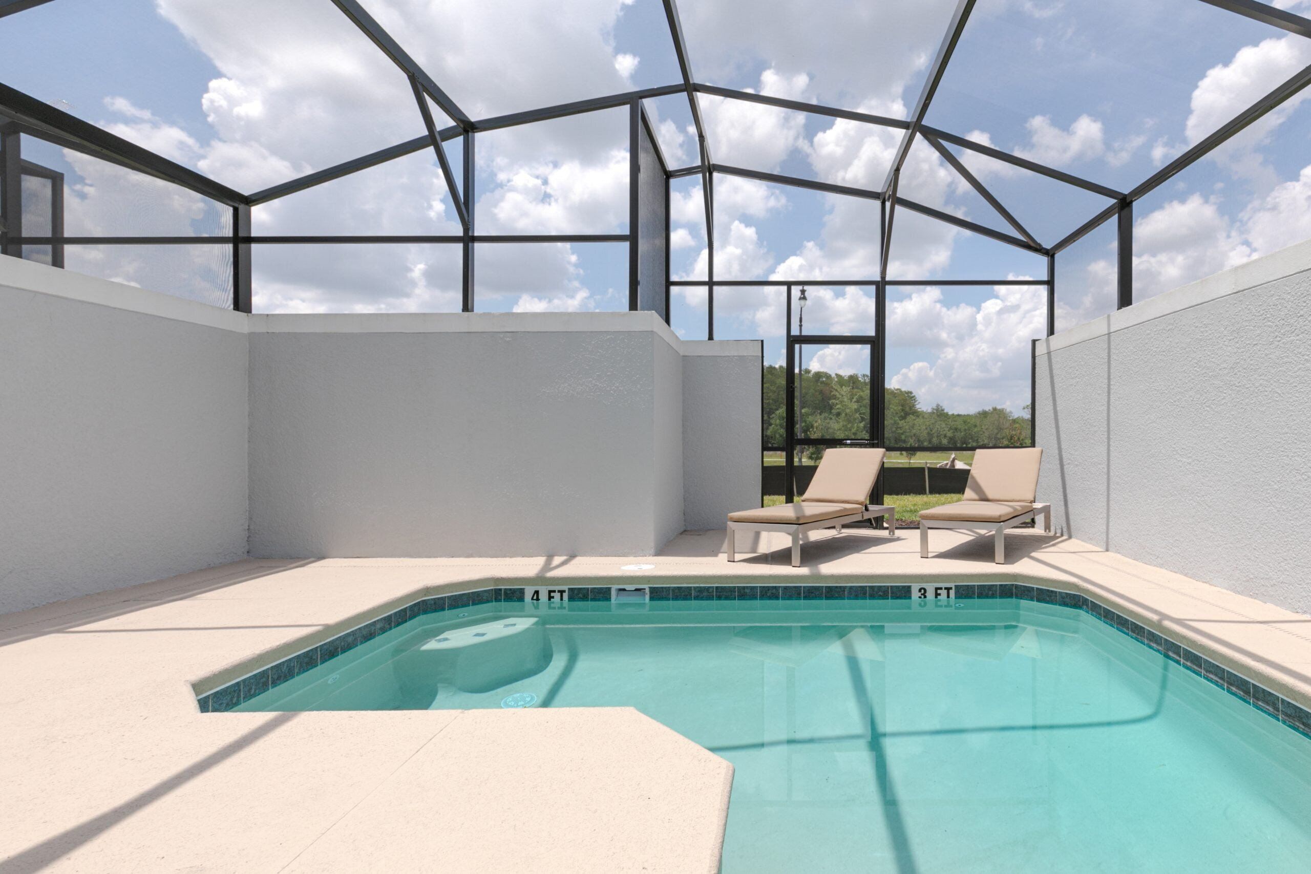 Ein heller, überdachter Pool mit Blick auf Himmel und Wolken, umgeben von einer weißen Wand und einer Metallkonstruktion. Zwei Liegestühle und ein kleiner Tisch am Poolufer sind vorhanden.