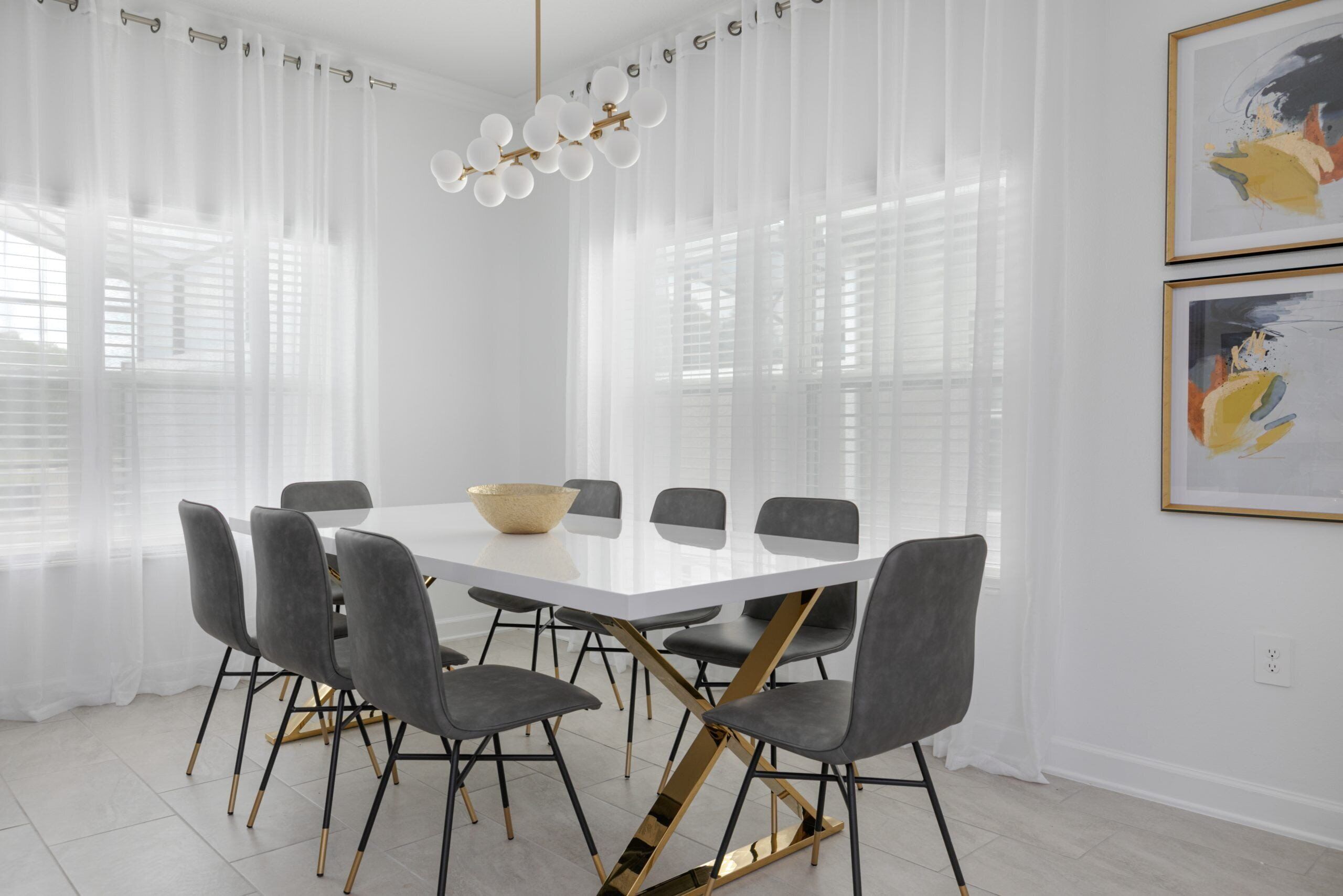 Un espace repas moderne avec une table blanche, des chaises grises et un pied de table doré.