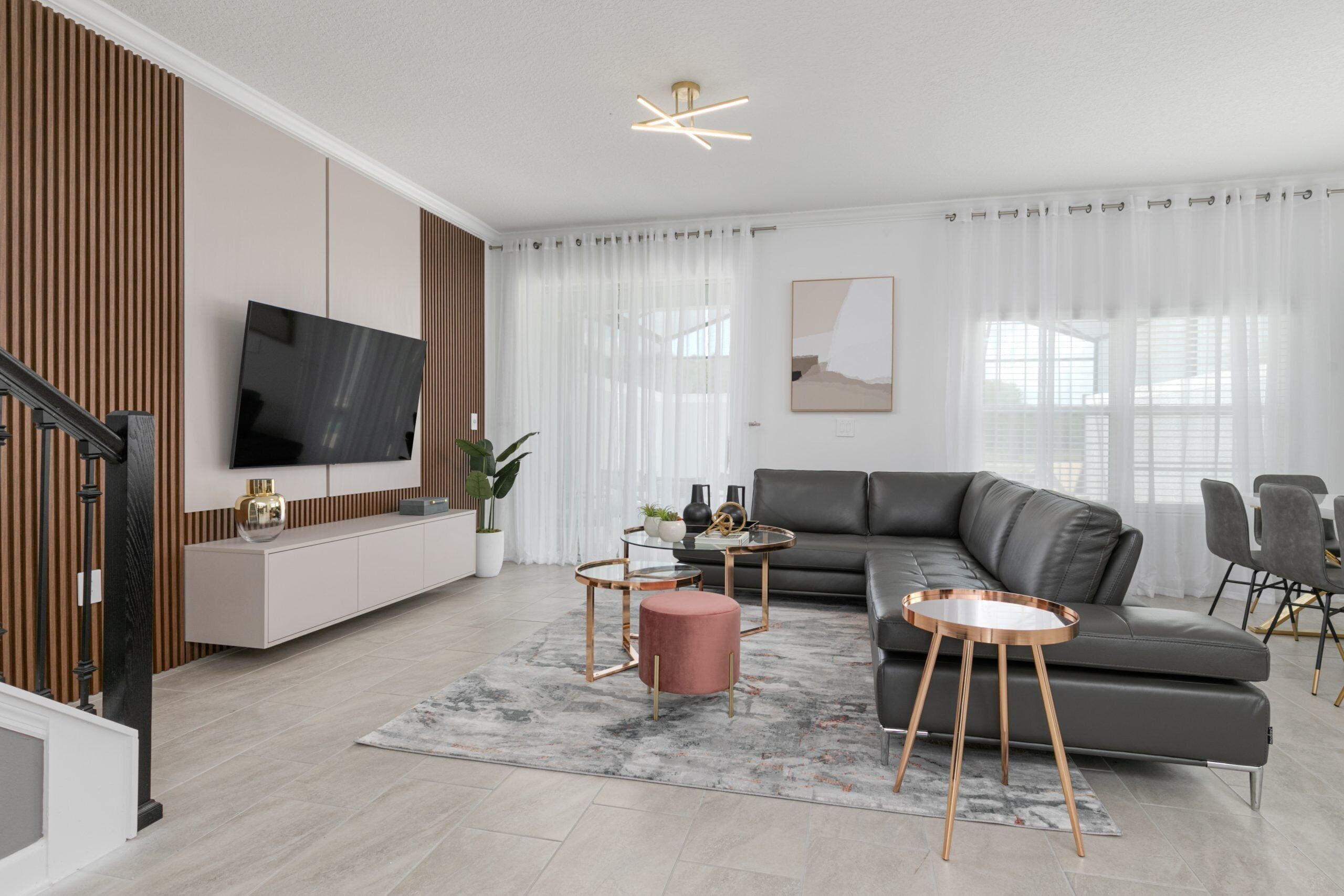 Ein modernes Wohnzimmer mit einer grauen Eckcouch, einem Flachbildfernseher, einem runden Couchtisch und einem roten Hocker.