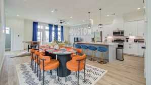 A modern kitchen with white cabinets, stainless steel appliances, and a central island with bar stools. - Rooftop Movie Oasis: 3bd - Games - Patio (Houston)