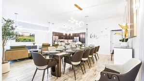 A modern kitchen with dark cabinetry, a central island, and a dining area with a long table and chairs. - Last Minute Disney! Private Pool, Hot Tub, Game Room & Themed Bedrooms. Book Now! #112541 (Orlando)