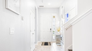 A hallway with white walls, a white door, a black and gold rug, and a small table with decorative items. - Last Minute Disney! Private Pool, Hot Tub, Game Room & Themed Bedrooms. Book Now! #112541 (Orlando)