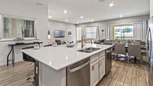 A modern kitchen with a central island, built-in appliances, and a dining area with a large window. - Last Minute Disney! Private Pool, Hot Tub, Game Room & Themed Bedrooms. Book Now! #112815 (Orlando)