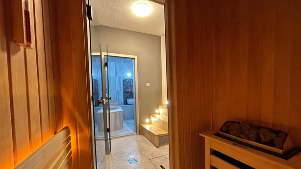 A hallway leading to a bathroom with a glass door, a wooden bench, and a small table with items on it.