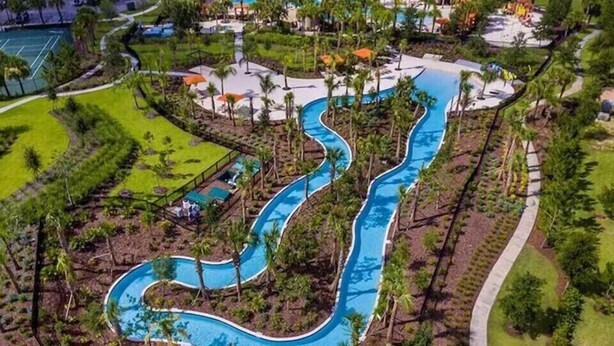 Vista aérea de um resort com piscina sinuosa, palmeiras e quadra de tênis.
