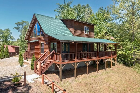 A log cabin with a green metal roof, a covered porch, and a wooden staircase leading to the entrance.