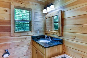 A wooden cabin bathroom with a sink, mirror, and window with blinds. - The Misty Blue Mountain Retreat (Murphy)