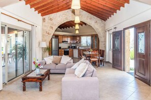 A spacious living area with a stone arch, a kitchen in the background, and a dining area with a wooden table and chairs.