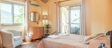 Un dormitorio con cama, una silla, cómoda, espejo y ventana con vista al exterior.