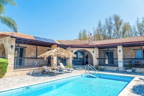 A pool area with a clear blue pool, lounge chairs, and a thatched umbrella.