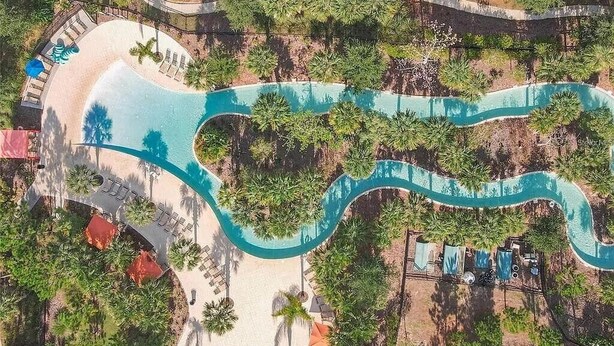 Vista aérea de un complejo turístico con una piscina serpenteante, palmeras y zonas de descanso.