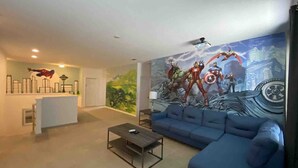 Una sala de estar moderna con un sofá azul, una mesita de centro, un mural con superhéroes y un mostrador de recepción blanco.